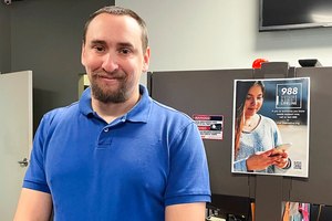988 Call Center Director Jamieson Brill poses for a photo in front of a desk where work workers take calls around the clock at a facility in Hyattsville, Md., on Oct. 7, 2022. Brill works in one of more than 200 call centers fanned out around the country.