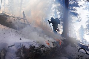 A member of the Mile High Youth Corps walks near a smoldering pile of tree debris during a controlled burn with the U.S. Forest Service in Hatch Gulch on Feb. 23, 2022, near Deckers, Colo. U.S. Agriculture Secretary Tom Vilsack said the forest service conducted burns, tree thinning and other work to reduce wildfire risks across 5,000 square miles last year.