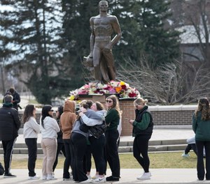 Students gather where flowers are being left at the Spartan Statue on the grounds of Michigan State University.
