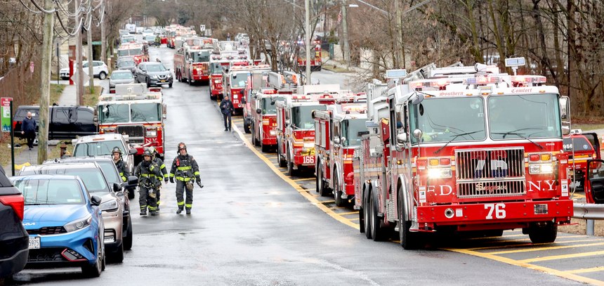 A line of fire trucks are parked along Woodrow Road as New York Firefighters battle a house fire.