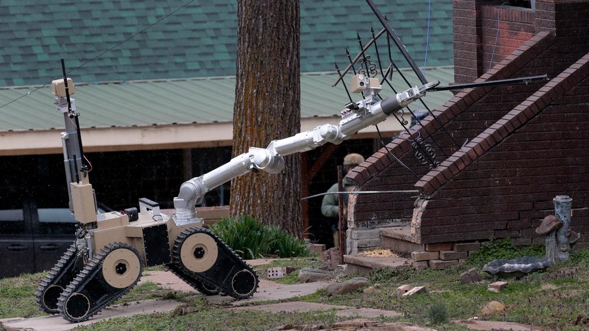 A robot removes the storm door of a home as tactical units from the Missouri Highway Patrol and St. Charles County police wait outside to search for a man accused of shooting two Hermann police officers Sunday night, on Monday, March 13, 2023, in Hermann, Mo. The St. Louis Post-Dispatch reported that police are focusing their search for a suspect Kenneth Lee Simpson on a home along Highway 19 near Hermann, not far from where the shooting happened.