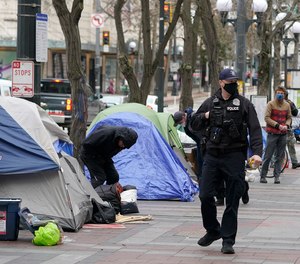 A Seattle police officer walks past tents used by people experiencing homelessness.