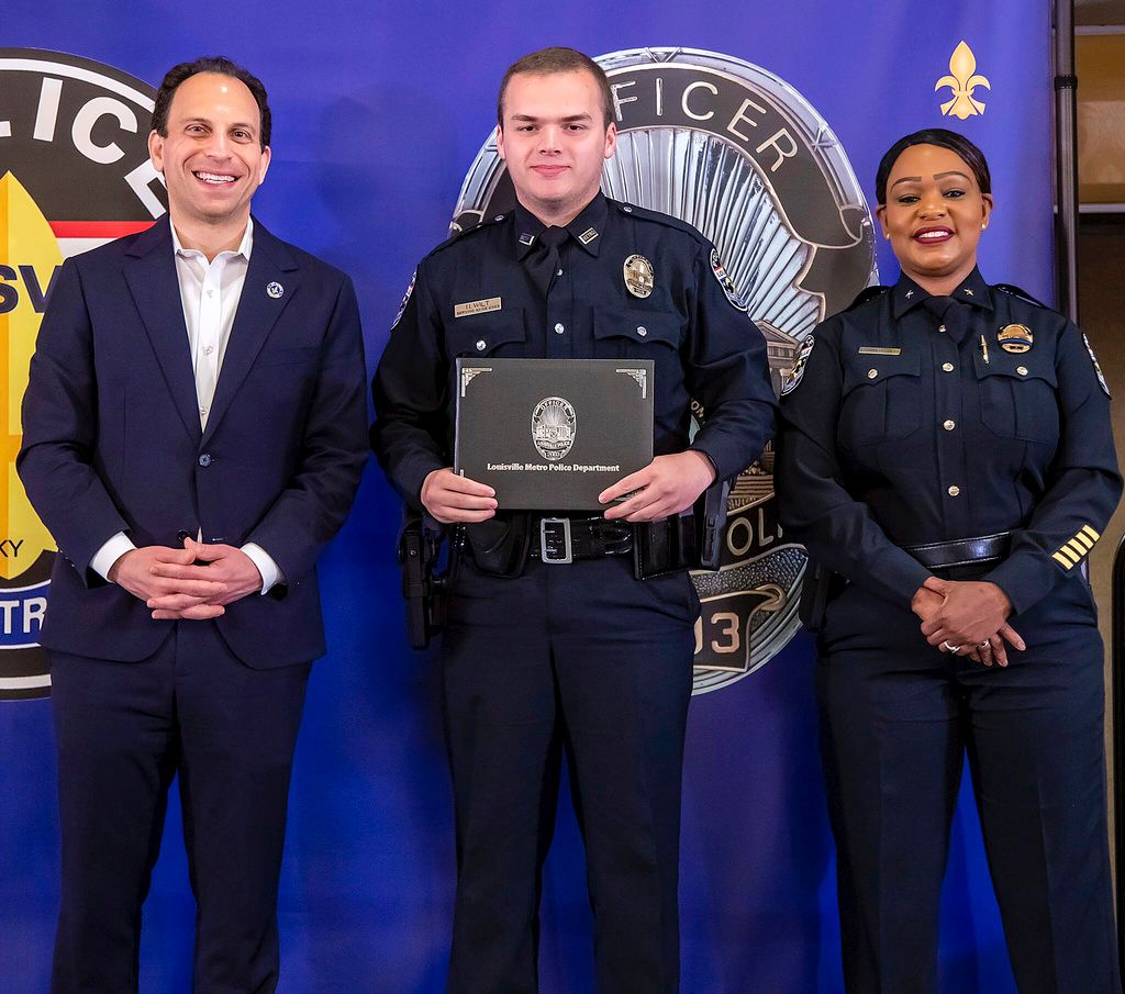 In this photo provided by the Louisville Metro Police Department, from left, Louisville Mayor Craig Greenberg, Officer Nickolas Wilt and Louisville Metro Interim Police Chief Jacquelyn Gwinn-Villaroel pose for a photo, in Louisville, Ky., March 31, 2023. Wilt was shot while responding to a call where a bank employee armed with a rifle opened fire at his workplace early Monday, April 10.