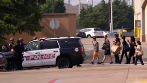 People raise their hands as they leave a shopping center following reports of a shooting, Saturday, May 6, 2023, in Allen, Texas.
