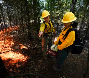 Instructor Ben McLane, left, helps teach Kerstin Joseph, right, as they start a prescribed fire during a wildland firefighter training.