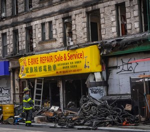 A firefighter looks through debris in the aftermath of a fire which authorities say started at an e-bike shop and spread to upper-floor apartments.