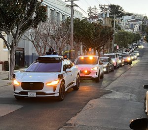 A Waymo driverless taxi stops on a street in San Francisco for several minutes because the back door was not completely shut, while traffic backs up behind it.