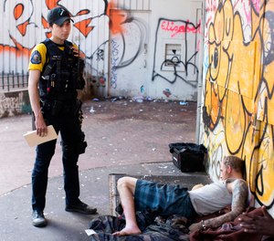 Officer Donny Mathew of the Portland Police Bureau's bike squad, stands next to a person who appears to be passed out on Thursday, May 18, 2023, in downtown Portland, Ore.
