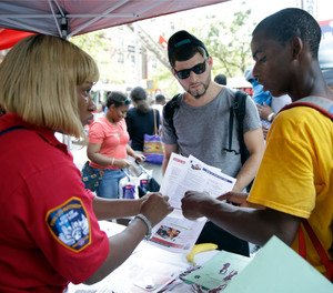In this Saturday, Aug. 15, 2015 photo, emergency medical technician Janice Gardner, left, talks to Kenneth Worrell, left, 16, and Steven Vargas, 23, while working the recruitment table during a FDNY block party in the Harlem neighborhood of New York.