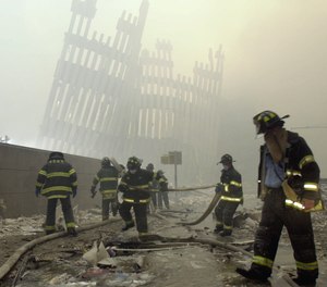 With the skeleton of the World Trade Center twin towers in the background, New York City firefighters work amid debris on Cortlandt St. after the terrorist attacks of Tuesday, Sept. 11, 2001.