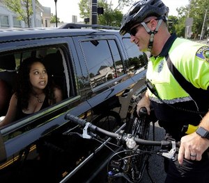 In this July 20, 2016 photo, police officer Matthew Monteiro speaks to a motorist about texting while driving while patrolling on his bicycle in West Bridgewater, Mass.