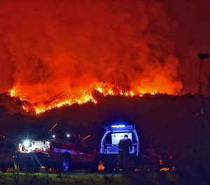 In this photo provided by the Santa Barbara County Fire Department, a Cal Fire firefighter looks over a map from the back of his truck parked off Bella Vista Drive above Montecito, Calif., as the fight against a wildfire continues Tuesday, Dec. 12, 2017.