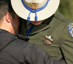 A black band covers the badge of California Highway Patrol Officer Jonathan Velazquez as he is comforted following a bell ringing ceremony held for CHP Officer Andrew Camilleri Sr., at the highway patrol academy Wednesday, Dec. 27, 2017, in West Sacramento, Calif.