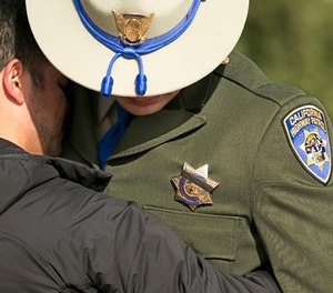 A black band covers the badge of California Highway Patrol Officer Jonathan Velazquez as he is comforted following a bell ringing ceremony held for CHP Officer Andrew Camilleri Sr., at the highway patrol academy Wednesday, Dec. 27, 2017, in West Sacramento, Calif. (AP Photo/Rich Pedroncelli)