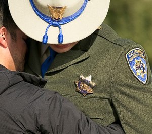 A black band covers the badge of California Highway Patrol Officer Jonathan Velazquez as he is comforted following a bell ringing ceremony held for CHP Officer Andrew Camilleri Sr., at the highway patrol academy Wednesday, Dec. 27, 2017, in West Sacramento, Calif. (AP Photo/Rich Pedroncelli)
