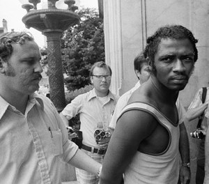 In this Sept. 1, 1973 photo, a federal marshal, left, escorts Herman Bell past members of the media following Bell's capture in New Orleans in connection with the killing of two New York city police officers. (AP Photo)