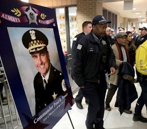 Chicago police officers pass a memorial portrait of Cmdr. Paul Bauer for a candlelight vigil for Bauer outside the Near North District headquarters Wednesday, Feb. 14, 2018, in Chicago. (AP Photo/Charles Rex Arbogast)