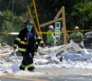 A firefighter walks through the scene of the LEAP building explosion that killed Farmington Fire Capt. Michael Bell and injured seven others on Monday, Sept. 16, 2019, in Farmington, Maine. Two companies have been fined for safety violations in connection with the deadly blast.