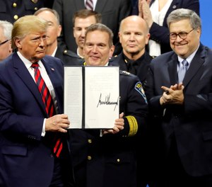 President Donald Trump is pictured at the 2019 IACP conference in Chicago after signing an executive order creating a commission to study law enforcement. Applauding on the right is Attorney General William Barr who recently said that the American people