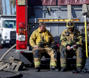 Firefighters rest with their fire truck at outside a cardboard box factory that burned down by a wildfire in Riverside, Calif. Thursday, Oct. 31, 2019. Some Calif. firefighters are turning to meditation, yoga and other therapies to avoid developing stress-related conditions.