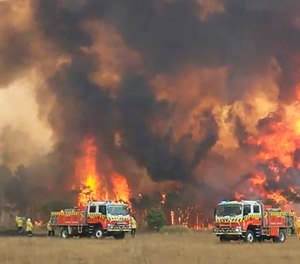 In this image dated Dec. 30, 2019, and provided by NSW Rural Fire Service via their Twitter account, firefighters are seen as they try to protect homes around Charmhaven, New South Wales. Wildfires burning across Australia's two most-populous states Tuesday trapped residents of a seaside town in apocalyptic conditions, destroyed many properties and caused fatalities.