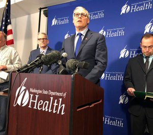 Washington Gov. Jay Inslee, center, speaks Tuesday Jan. 21, 2020, at a news conference in Shoreline, Wash., following the announcement that a man in Washington state is the first known person in the United States to catch a new type of coronavirus that officials believe originated in China. A U.S.-based international standard-setting agency for emergency dispatchers has released guidelines for screening callers for potential exposure to the virus.