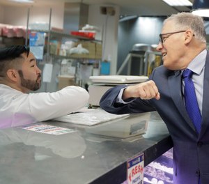 Washington Gov. Jay Inslee, right, bumps elbows with a worker at the seafood counter of the Uwajimaya Asian Food and Gift Market, Tuesday, March 3, 2020, in Seattle's International District.