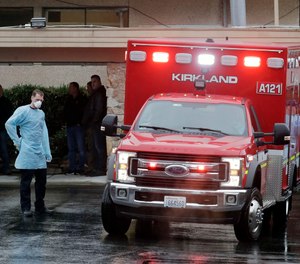 Workers stand near an ambulance, Friday, March 6, 2020, at the Life Care Center in Kirkland, Wash., which has become the epicenter of the COVID-19 coronavirus outbreak in Washington state.