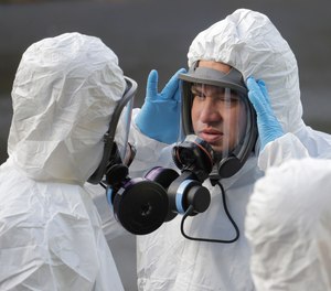 A worker from a Servpro disaster recovery team wearing a protective suit and respirator adjusts his mask before entering the Life Care Center in Kirkland, Wash. to begin cleaning and disinfecting the facility, Wednesday, March 11, 2020, near Seattle. The nursing home is at the center of the outbreak of the COVID-19 coronavirus in Washington state.