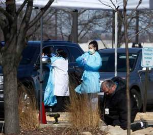 Medical staff wearing safety garments assist a driver at a new coronavirus drive-up test clinic.