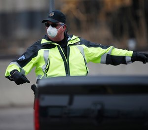 A Denver Police Department officer wears a surgical mask while directing traffic at a coronavirus drive-through testing site outside the Denver Coliseum Saturday, March 14, 2020, in Denver. Officials planned to administer 150 tests but the line of vehicles wrapped around three city blocks.