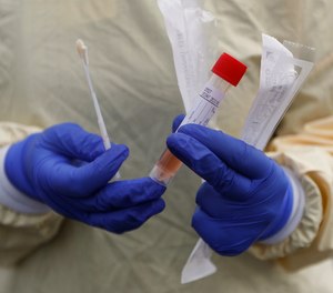 A nurse holds swabs and test tube to test people for COVID-19 at a drive through station. In Massachusetts, EMS providers are being trained to soon provide at-home COVID-19 testing across the state.