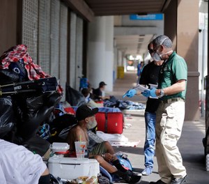 The Miami-Dude County Homeless Trust's chair, Ron Book, left, accompanied the City of Miami Homeless Services Division assistant program administrator Lazaro Trueba, right, talk to a homeless man about washing his hands during the COVID-19 virus outbreak in downtown Miami, on Friday, March 20, 2020.