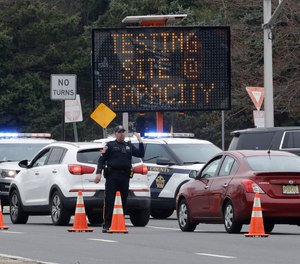 A police officer waves traffic past the entrance to a drive-thru COVID-19 testing center after it reached capacity in Paramus, N.J., Friday, March 20, 2020.