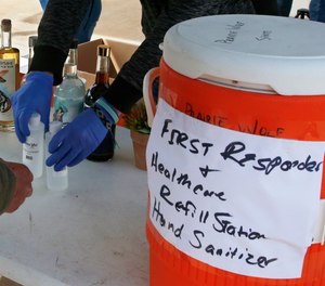 A customer buys two 8 oz. bottles of hand sanitizer at the Prairie Distillery, which has switched from making liquor to making hand sanitizer due to the coronavirus pandemic, in Guthrie, Okla., Saturday, March 21, 2020. The bottles of liquor, which are their usual production item, are not for retail sale. The large container at right allows first responders and healthcare professionals to refill containers of hand sanitizer for free.
