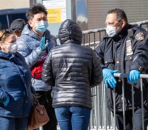A police officer talks to people who have arrrived to line up outside Elmhurst Hospital Center to be tested for the coronavirus, Tuesday, March 24, 2020, in the Queens borough of New York.