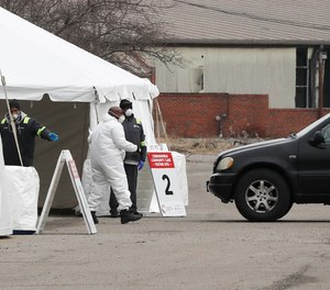 Healthcare officials watch as a vehicle approaches a testing site at the Michigan State Fairgrounds, Friday, March 27, 2020, in Detroit. Detroit and Wayne County officials are considering hazard pay for first responders and other front-line workers during the COVID-19 pandemic.
