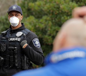 Seattle Police officer Rosell Ellis, left, wears an N95 mask and stands at a distance as he listens to a man officers made contact with during a routine call Thursday, April 2, 2020, in Seattle. (AP Photo/Ted S. Warren)