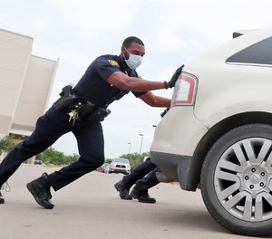 Amid concerns of the spread of COVID-19, Dallas ISD police officer Mylon Taylor helps push a car that ran out of gas while waiting in line for the weekly school meal pick up for students in Dallas, Thursday, April 9, 2020.