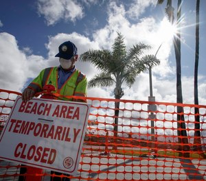 A city worker puts up signs to close part of the beach in Newport Beach, Calif., Friday, April 10, 2020. 