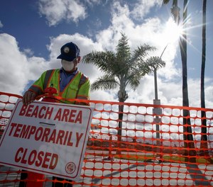 A city worker puts up signs to close part of the beach in Newport Beach, Calif., Friday, April 10, 2020.