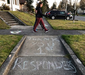 In this April 9, 2020 photo, pedestrians on an evening walk in Tacoma, Wash., stroll past a message written in sidewalk chalk thanking first responders serving the public during the coronavirus outbreak.