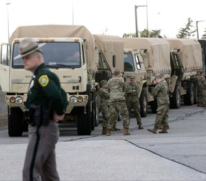 A New Hampshire State Police trooper stands by as members of the New Hampshire National Guard prepare to transport PPE delivered to Manchester-Boston Regional Airport, in Manchester, N.H., by a FedEx cargo plane.