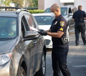 Surfside, Fla. Police Sgt. Jay Matelis, right, hands out a pair of cloth protective masks to a resident as she drives through, Monday, April 13, 2020, in Surfside.