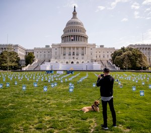 A man stops to take a photograph as he walks his dog past a thousand signs made by the advocacy group MoveOn along with other organizations that read #GetUsPPE, on the West Lawn of the U.S. Capitol, Friday, April 17, 2020, in Washington. U.S. Rep. Matt Cartwright has unveiled a proposal to provide hazard pay to front-line workers, including first responders and healthcare professionals, during the COVID-19 pandemic.