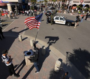 A protester, center foreground, stands with a flag as police block off an intersection during a demonstration against stay-at-home orders that were put in place due to the COVID-19 outbreak, Friday, April 17, 2020, in Huntington Beach, Calif.