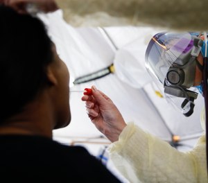 In this April 20, 2020 photo, Catherine Hopkins, Director of Community Outreach and School Health at St. Joseph's Hospital, right, performs a test on a patient in a COVID-19 triage tent at St. Joseph's Hospital in Yonkers, N.Y. The state of New York is hiring thousands of contact tracers in its effort to slow the spread of the virus.