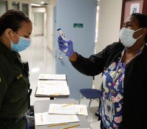 In this April 16, 2020, photo Sonia Munoz, left, custody assistant, gets her temperature taken at the hospital ward of the Twin Towers jail in Los Angeles.