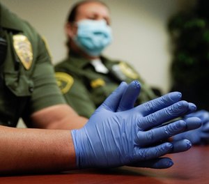 In this April 16, 2020, photo Christopher Lumpkin's gloved hands are shown during an interview at the hospital ward of the Twin Towers jail in Los Angeles. Across the country first responders who've fallen ill from COVID-19, recovered have begun the harrowing experience of returning to jobs that put them back on the front lines of America's fight against the novel coronavirus.