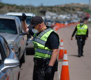 New Mexico state police officers screen cars for compliance with an emergency lockdown order that bans nonessential visitors and limits vehicle passengers to two people as they enter Gallup, N.M., Thursday, May 7, 2020.